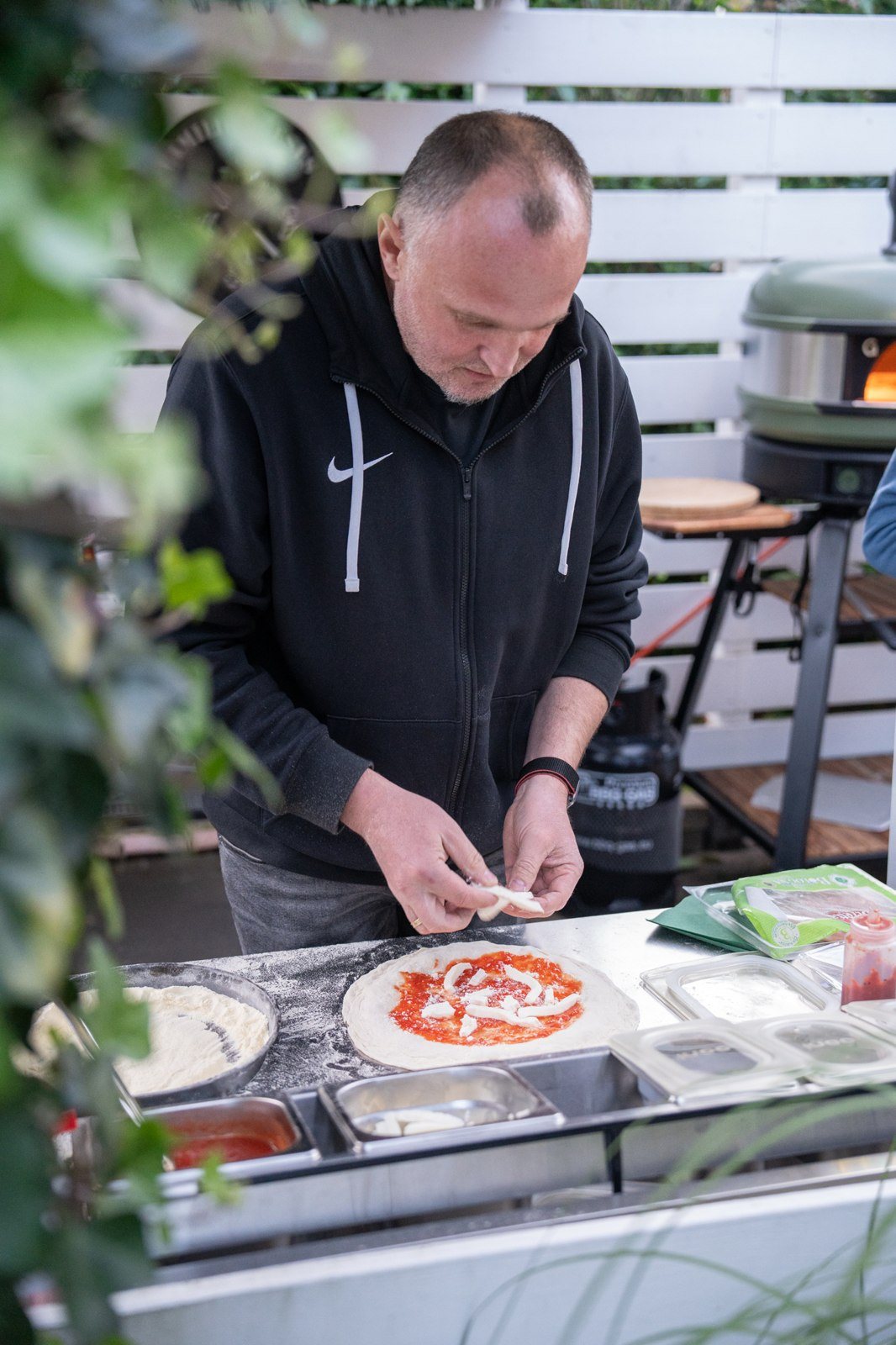 Eine Pizza wird draußen am vorbereiteten Tisch belegt.