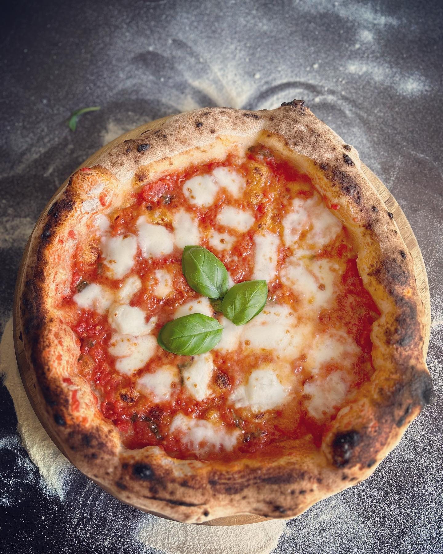 Eine neapolitanische Margherita mit Tomate, Mozzarella und Basilikum auf einer bemehlten Arbeitsfläche.