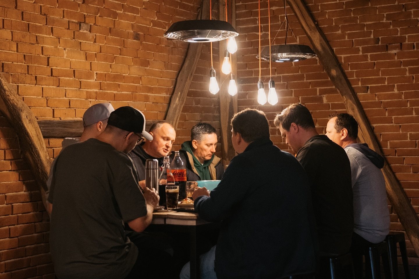 Eine Gruppe sitzt beim gemeinsamen Pizza-Abend um einen hohen Tisch in einer Backsteinscheune.
